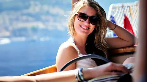 Person wearing sunglasses smiles with her hand in her hair.