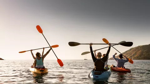 People in kayaks holding their paddles in the air.