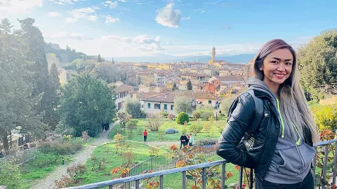 Person leans against fence while smiling in the Giardino delle Rose in Florence with a view of the city behind.