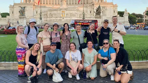 Small group of people posing together in front of the Altare della Patria in Rome.