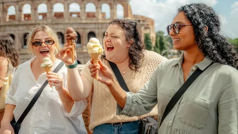  Three people smiling while holding gelato in front of the Roman Colosseum.