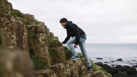 Person climbs up the large stones that make up the Giant’s Causeway.