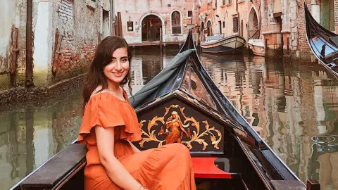 Person sitting inside a gondola boat on a quiet canal in Venice, Italy.