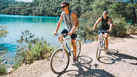 Two people cycling along a path near a body of water in Europe.