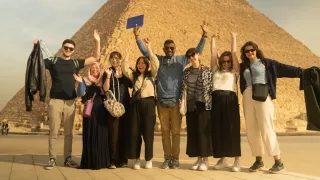 Group of people smiling with their hands in the air in front of an Egyptian pyramid.