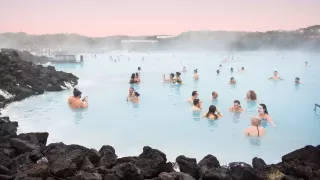 People soaking in Blue Lagoon with pink sky on the horizon.