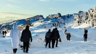 Group of people walk through a snow-covered landscape with sharp rock formations.