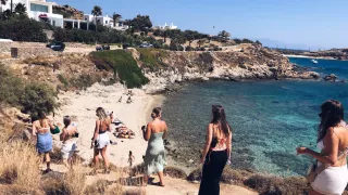 People walk down a hill towards a beach in Mykonos.