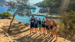 Seven people standing on a hill in the sun with the ocean and boat dock behind them.