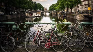 A lone bike leaning on the railing of a road looking out over one of the canals in Amsterdam.
