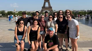 Small group of people pose together in front of the Eiffel Tower in Paris.