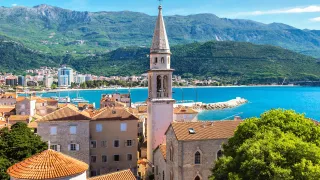 View of the coastal town of Budva with its orange rooves and nearby mountain range.