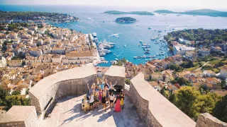 Group of people standing together with their hands in the air on a panoramic view point above Hvar Town on Hvar Island.