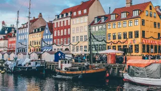 Wooden sail boats docked in canal lined with brightly coloured houses.