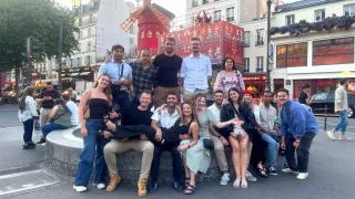 Group of peoppe pose together in front of the Moulin Rouge cabaret in Paris.