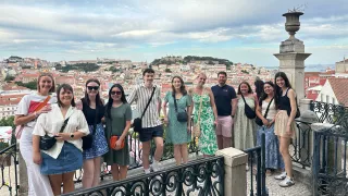 People standing together shoulder to shoulder for a photo in front of the cityscape of Lisbon, Portugal.