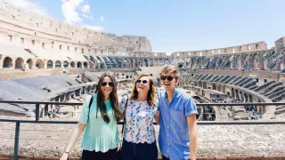 Three people stand together smiling while standing inside the Colosseum in Rome.