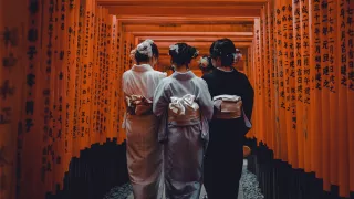 Three people wearing kimonos walk through the torii gates of the Fushimi Inari Shrine in Kyoto, Japan.
