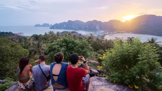 People sitting together on a large rock watching the sunrise in the Phi Phi Islands.