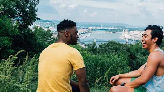 Two male Topdeck travelers laughing and joking with each other with a landscape view of Budapest in the background.