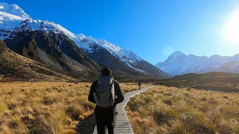 Man walking down a walkway with mountains and a bright blue sky in the background