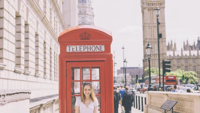 A woman standing in front of a red telephone box, with Big Ben in the background