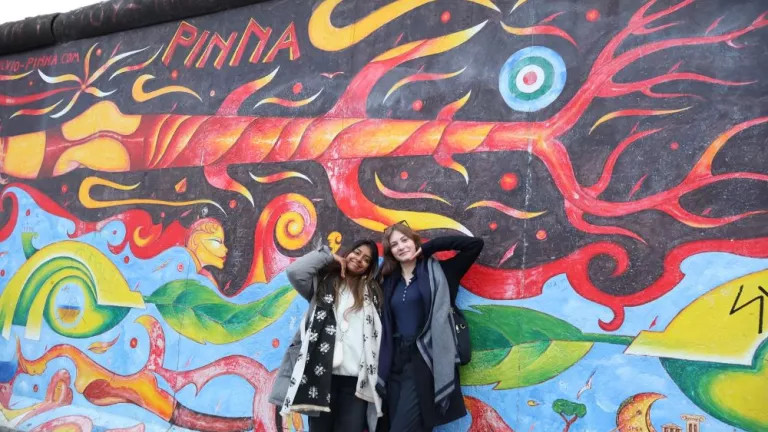 Two women standing in front of a wall of painted art