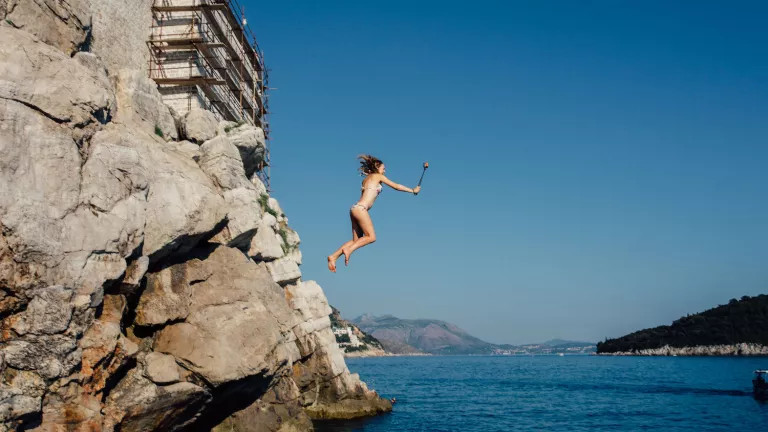 woman jumping off rocks into water
