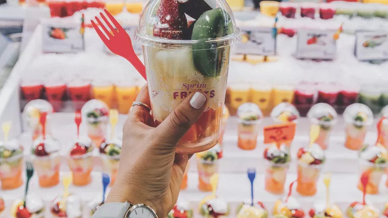 Person holding a plastic pot of fruit in front of a counter where all the pots of fruits are being displayed