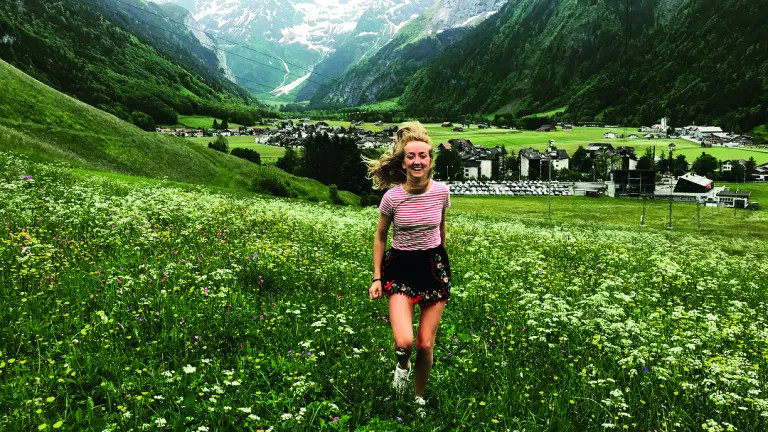 A woman running through a field of flowers, with Swiss mountains in the background