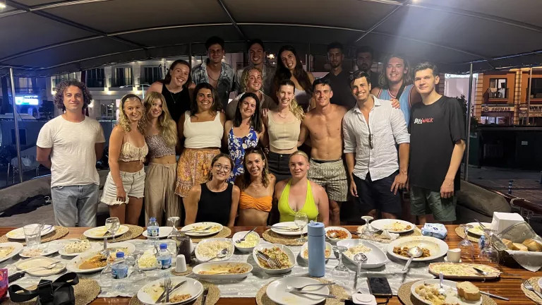 large group of people smiling and standing behind a table of food
