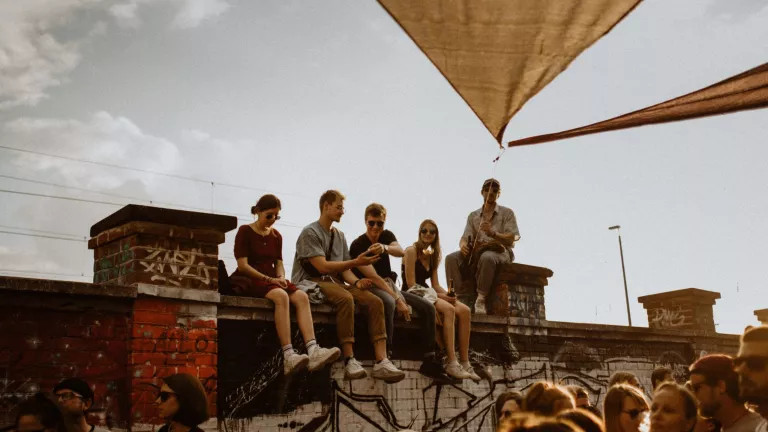 A group of people sitting on top of a wall, with a crowd below them