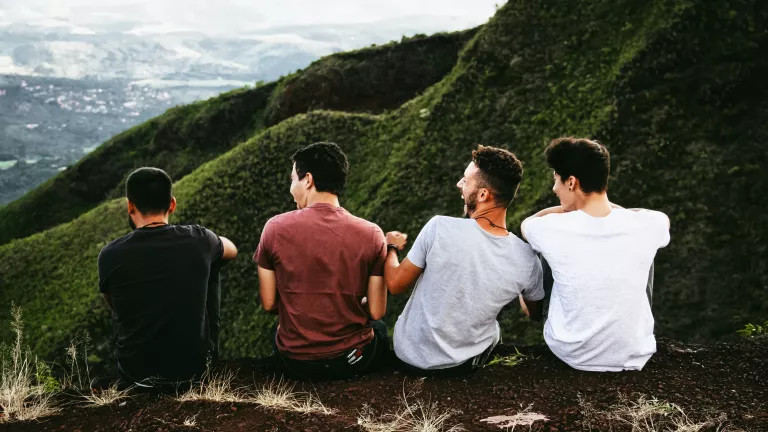 four men sitting away from the camera laughing. They are sat on a mountain