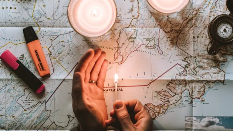 a hand holding a match to a map with candles around it