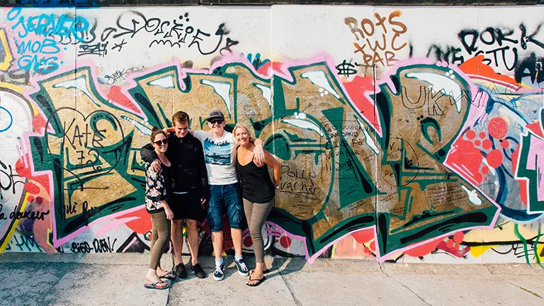 Small group of people standing in front of a wall covered in colourful graffiti street art.