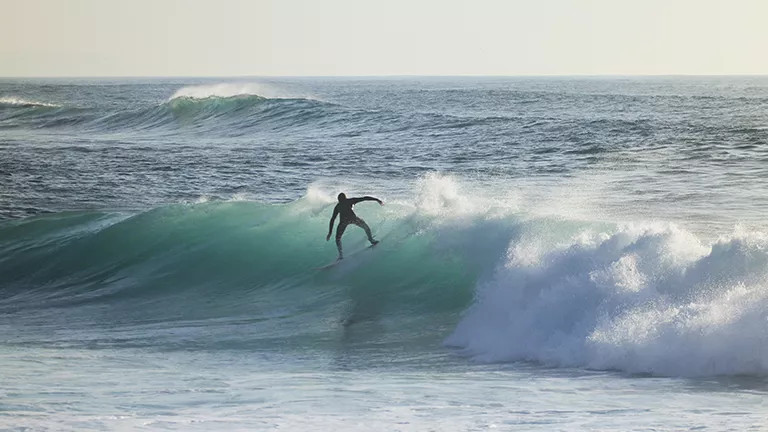Person on a surfboard rides a wave as it begins to break.
