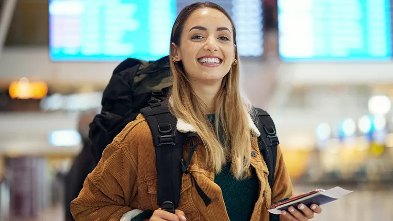 Person smiles with backpack and passport in airport.