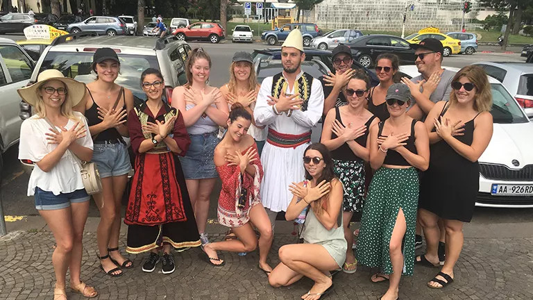 Group of people posing together with their hands in front of their chest, thumbs interlocked.