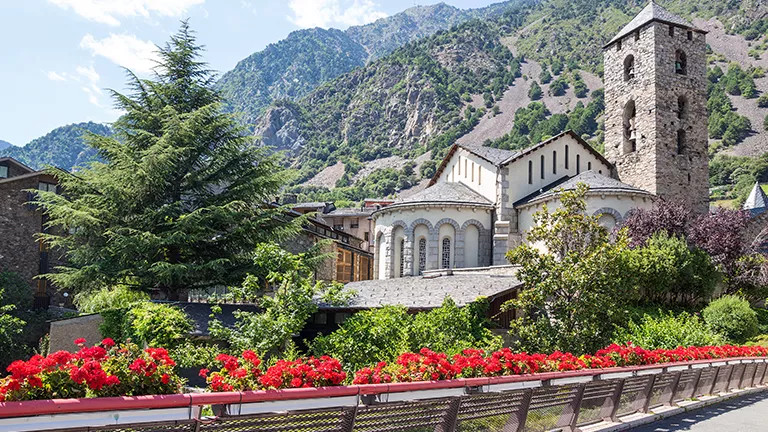 Building with stone tower against with rocky mountain background behind.