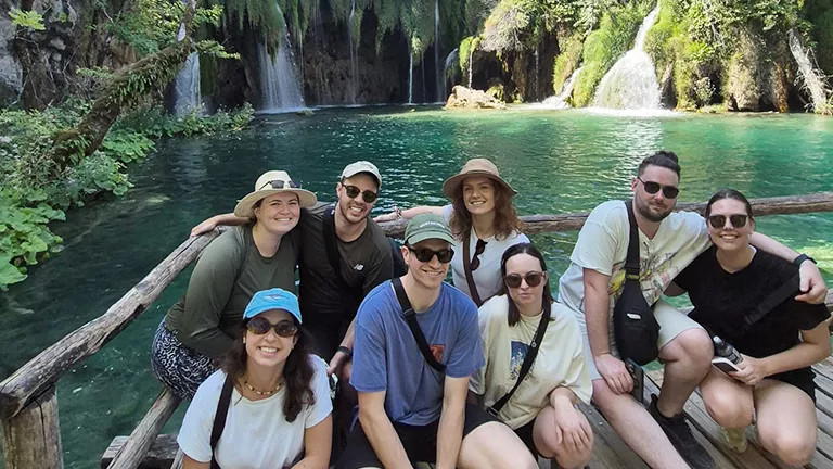 People crouching down for a photo together near a pond with waterfalls in a national park.