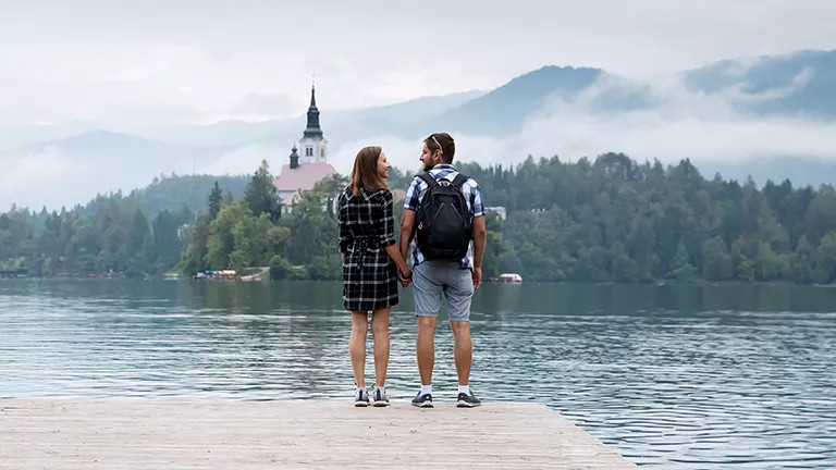 Two people holding hands while looking at each other in front of Lake Bled.