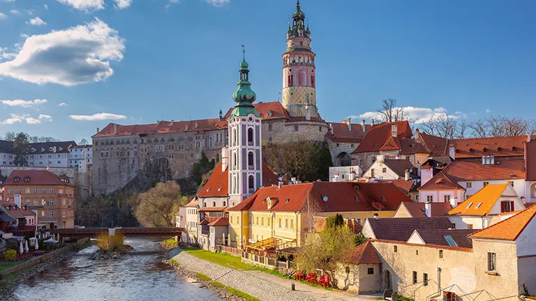 Orange roof buildings and the Český Krumlov Castle along a river.