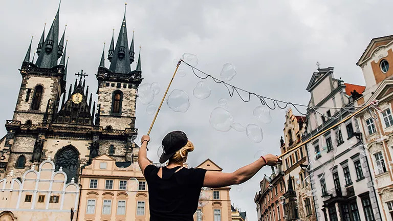 Person using bubble blower in Prague’s Old Town Square with the Church of Our Lady before Týn behind.