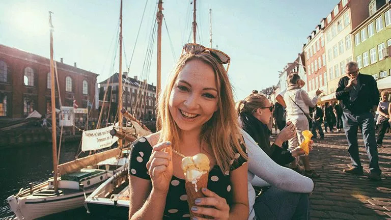 Person holding gelato in a cone on street next to canal.