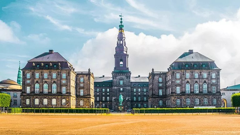 Large stone building with tower in the center known as Christiansborg Palace.