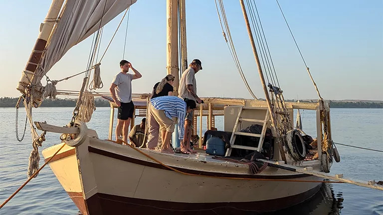 People standing on the bow of a traditional felucca boat on the Nile River.