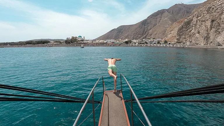 Person diving off the bow of a sail boat in the Greek Islands.