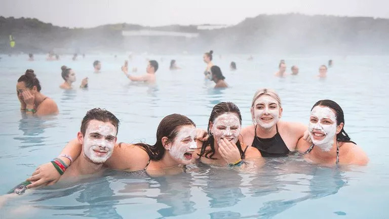 Group of people stand in Iceland’s Blue Lagoon with must masks on their faces and their arms around each others shoulders.