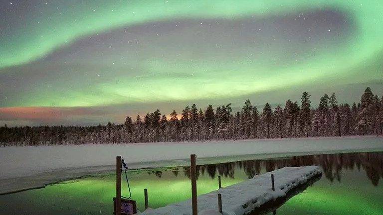 Aurora Borealis lights up the night sky, reflecting on a frozen lake below.