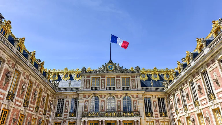 The traditional building of the Palace of Versailles with the French flag flying.